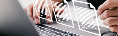 Eine Person sitzt vor einem Laptop. Über dem Laptop schweben Piktogramme von Dokumente auf einer virtuellen Ebene und werden von der Person bearbeitet.