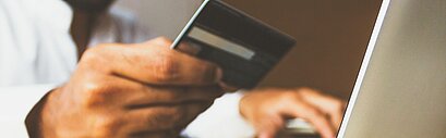 Ein Mann der in seiner rechten Hand eine Kreditkarte hält und mit der linken Hand ein Laptop bedient.