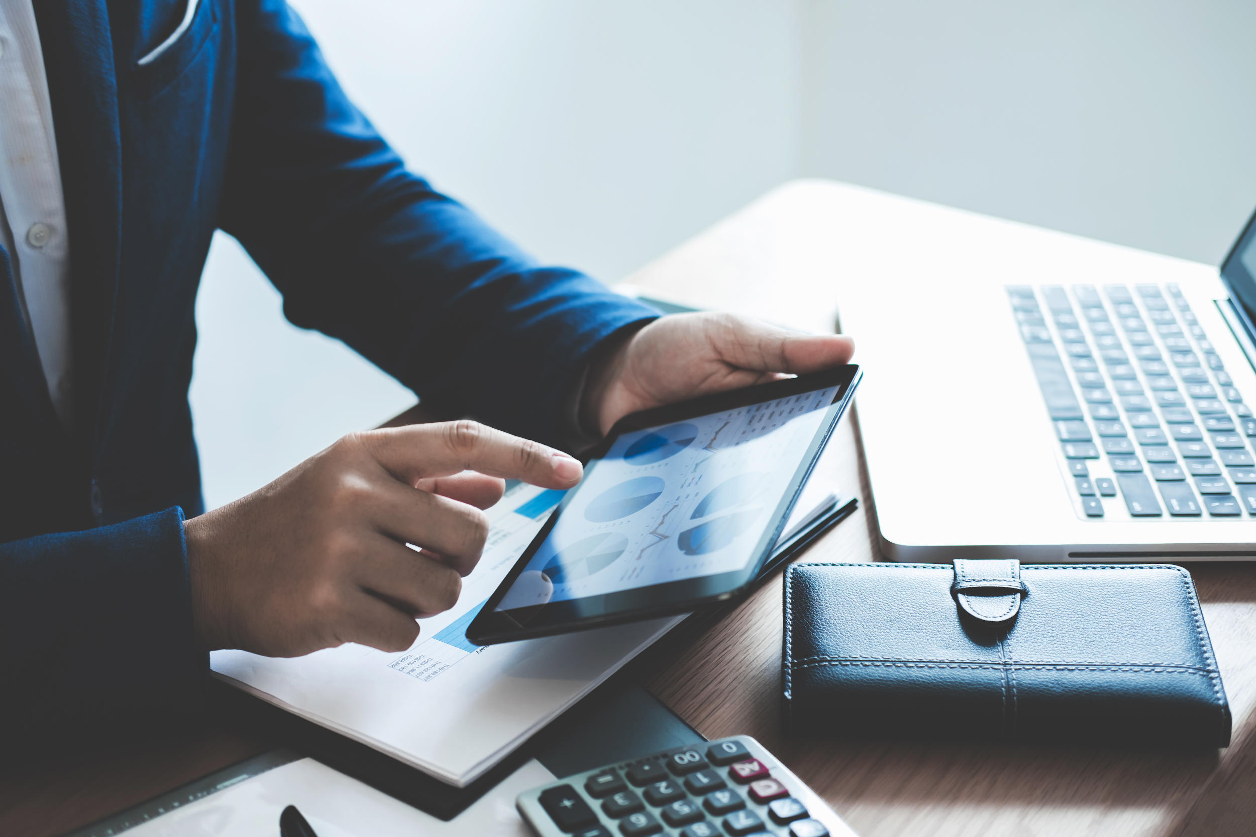 Ein Mann verwaltet digitale Daten auf einem Tablet, daneben steht ein Laptop.