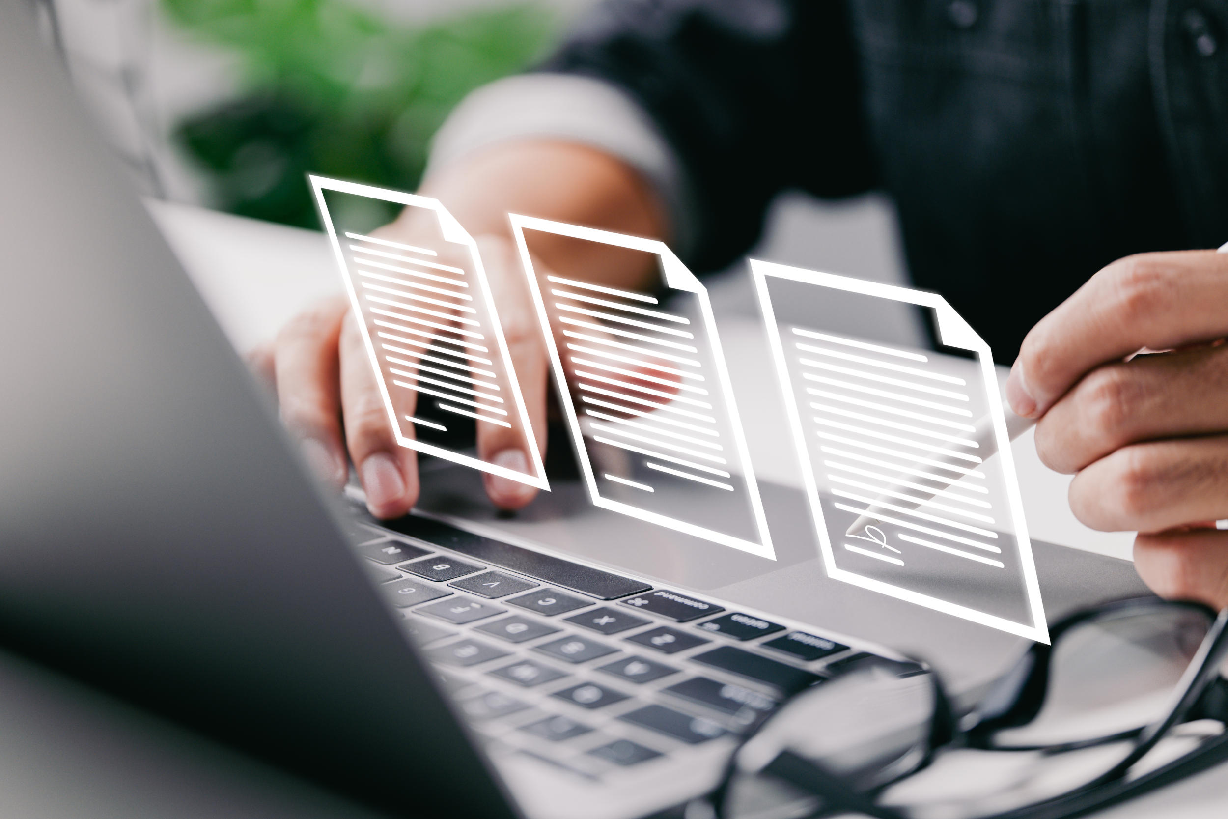 Eine Person sitzt vor einem Laptop. Über dem Laptop schweben Piktogramme von Dokumente auf einer virtuellen Ebene und werden von der Person bearbeitet.